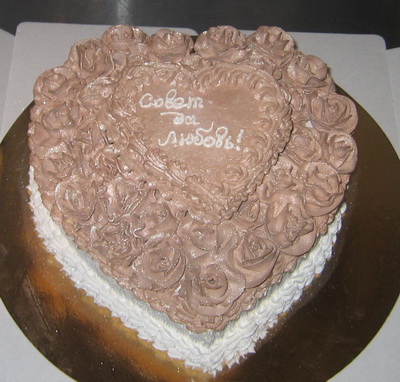 Свадебный торт кремового цвета в виде сердца украшен сливками розы